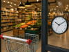 Ulaz u supermarket s praznim kolicima i satom na staklenim vratima, unutrašnjost trgovine u pozadini.