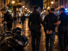 Policija privodi mladića na noćnoj gradskoj ulici dok se u blizini odvija sukob muškarca i žene kraj motocikla.