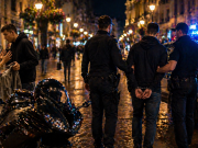 Policija privodi mladića na noćnoj gradskoj ulici dok se u blizini odvija sukob muškarca i žene kraj motocikla.