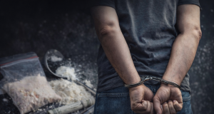 Ruke u lisicama s drogom u pozadini