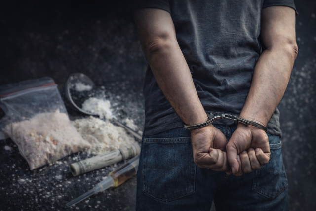 Ruke u lisicama s drogom u pozadini Ruke u lisicama s drogom u pozadini