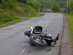 Srušeni motocikl leži na kolniku nakon prometne nesreće na zavoju ceste, bez vidljivih sudionika.