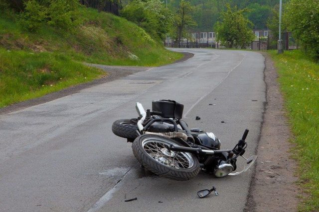 Srušeni motocikl leži na kolniku nakon prometne nesreće na zavoju ceste, bez vidljivih sudionika.