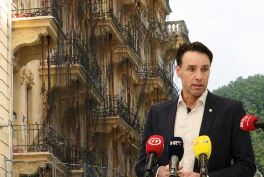 Gradonačelnik Fernando Kirigin govori na konferenciji za medije, u pozadini zgrada u Opatiji s postavljenim skelama i zaštitnim mrežama.