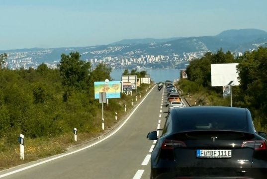 Kolona vozila na cesti prema unutrašnjosti s pogledom na Kvarner i Rijeku u pozadini